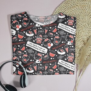 May include: Black t-shirt with a repeating pattern of Hello Kitty characters, cupcakes, ice cream cones, and candies. The shirt includes the text "Hello Kitty" and "You have a way of brightening my day!"