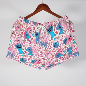 Puede incluir: Shorts blancos con cintura con cord&oacute;n, con un estampado repetido de personajes de dibujos animados azules y rosas, corazones y la palabra "LOVE". Los shorts cuelgan de una percha de madera.