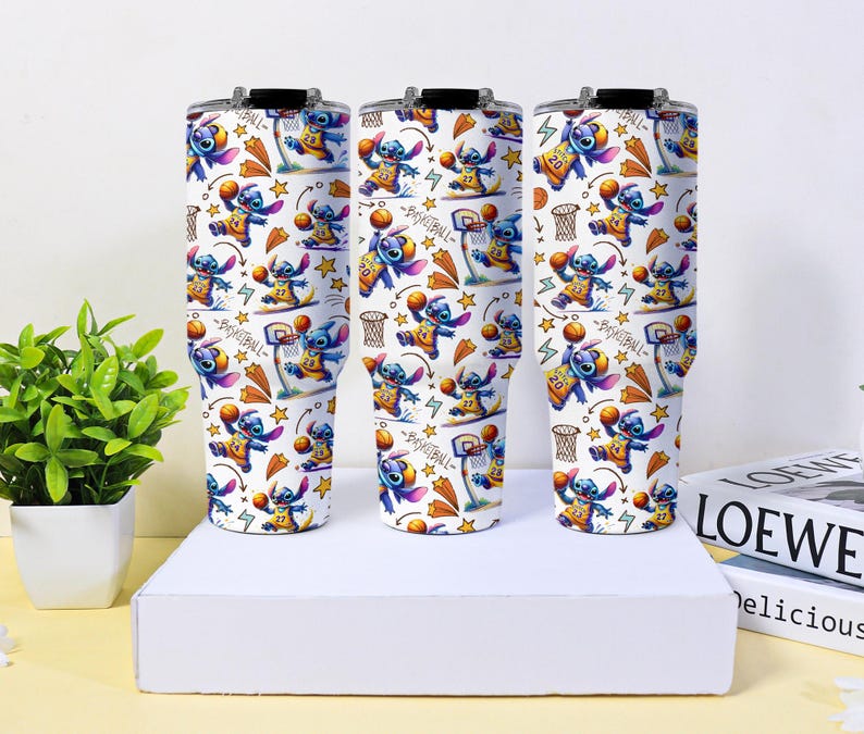 May include: Three white insulated tumblers with black lids. Each tumbler features a repeating pattern of the character Stitch playing basketball, with basketball hoops, stars, and basketballs. The text "Basketball" is also visible.