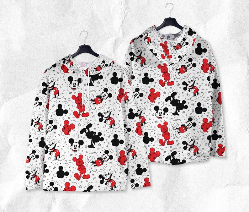 May include: Two white sweatshirts featuring a repeating pattern of Mickey Mouse in red and black. The sweatshirts are displayed on black hangers against a white backdrop. The pattern includes Mickey Mouse figures, stars, and Mickey Mouse head silhouettes.