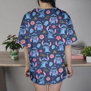 Pu&ograve; includere: Abito a maglietta blu navy con un motivo ripetuto del personaggio Stitch di Lilo & Stitch, fiori rosa e foglie verdi. L'abito &egrave; a maniche corte e ha una vestibilit&agrave; ampia.