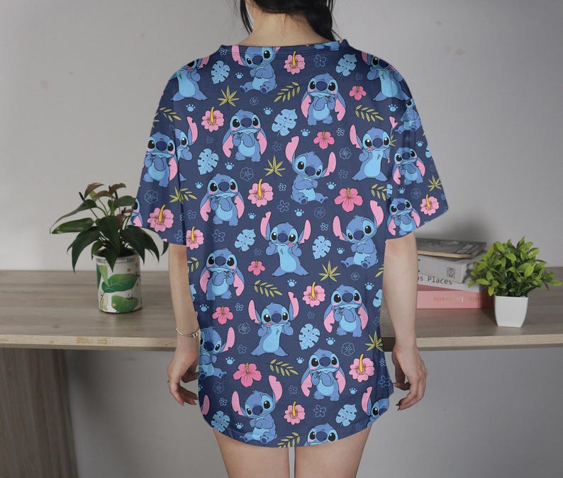 Pu&ograve; includere: Abito a maglietta blu navy con un motivo ripetuto del personaggio Stitch di Lilo & Stitch, fiori rosa e foglie verdi. L'abito &egrave; a maniche corte e ha una vestibilit&agrave; ampia.