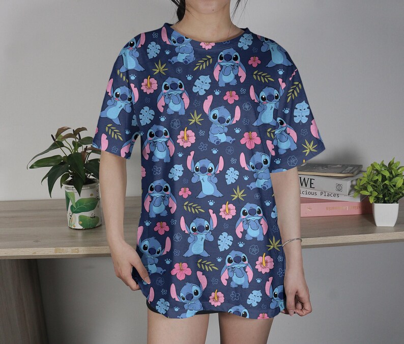 Pu&ograve; includere: Una maglietta blu navy con un motivo ripetuto del personaggio Stitch di Lilo & Stitch, fiori rosa e foglie verdi. La maglietta ha maniche corte e una vestibilit&agrave; ampia.