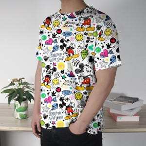 May include: White t-shirt featuring a repeating pattern of Mickey Mouse, stars, hearts, and speech bubbles. The shirt includes the phrases "Mickey Mouse", "Here we go!", and "You know I'm right!" in a playful design.