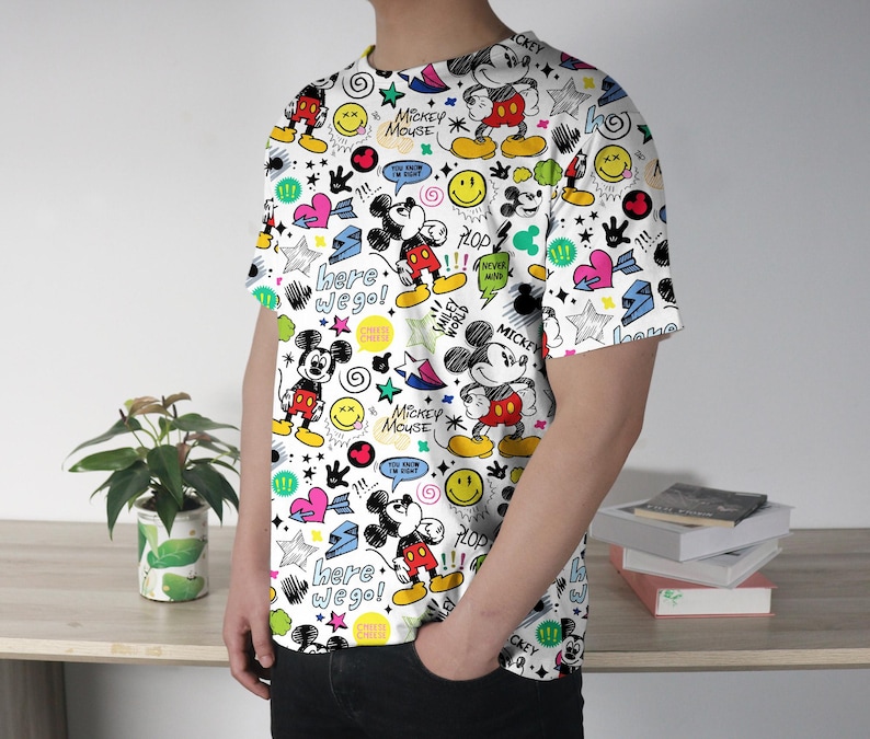 May include: White t-shirt featuring a repeating pattern of Mickey Mouse, stars, hearts, and speech bubbles. The shirt includes the phrases "Mickey Mouse", "Here we go!", and "You know I'm right!" in a playful design.