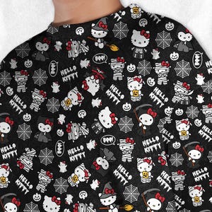 May include: Black long-sleeve shirt with a repeating Halloween-themed pattern. The design features Hello Kitty characters dressed as mummies, vampires, and witches, along with spiderwebs, pumpkins, and the text "HELLO KITTY".