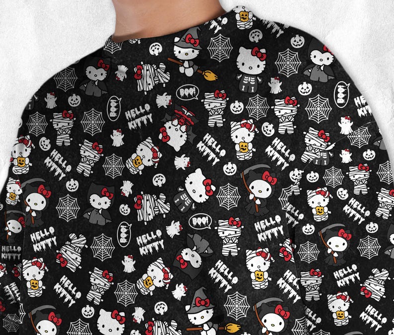 May include: Black long-sleeve shirt with a repeating Halloween-themed pattern. The design features Hello Kitty characters dressed as mummies, vampires, and witches, along with spiderwebs, pumpkins, and the text "HELLO KITTY".