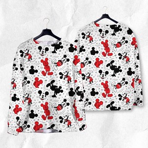 May include: White long-sleeved sweatshirt with a repeating pattern of Mickey Mouse in red and black, and black Mickey Mouse silhouettes. The design includes small stars and hearts. The sweatshirt is displayed on a black hanger.