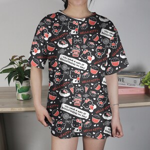 May include: Black t-shirt dress with a repeating pattern of Hello Kitty characters, cupcakes, ice cream cones, and bows in red and white. The text "HELLO KITTY" and "YOU HAVE A WAY OF BRIGHTENING MY DAY!" are also featured.