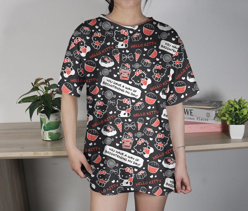 May include: Black t-shirt dress with a repeating pattern of Hello Kitty characters, cupcakes, ice cream cones, and bows in red and white. The text "HELLO KITTY" and "YOU HAVE A WAY OF BRIGHTENING MY DAY!" are also featured.