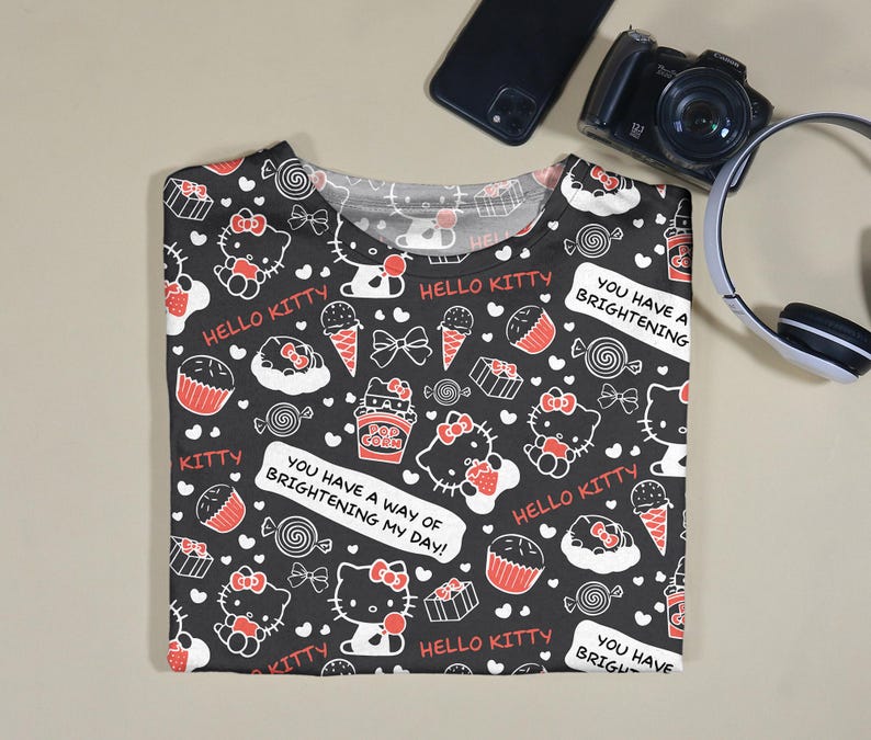 May include: Black t-shirt with a repeating pattern of Hello Kitty characters, sweets, and text. The design includes red, white, and black elements. Text on the shirt reads "Hello Kitty" and "You have a way of brightening my day!"