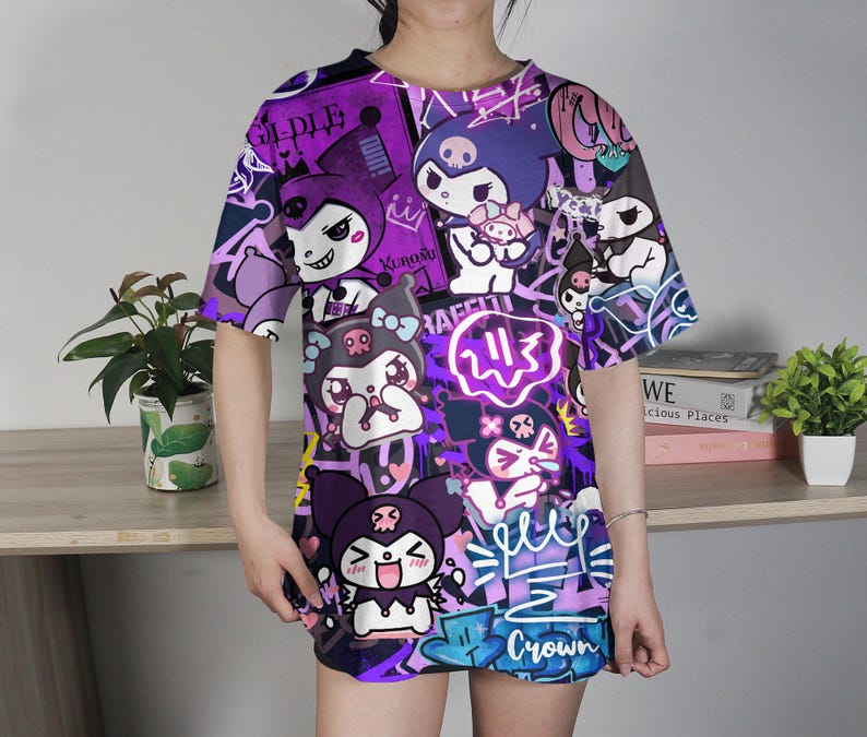 May include: Oversized purple t-shirt with a colourful all-over print of cartoon characters in different poses. The design includes graffiti art, with the word "Crown" visible. The shirt has short sleeves and a crew neck.