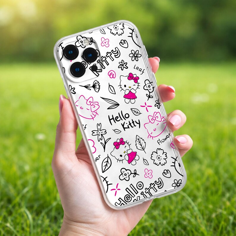 May include: Clear phone case with a white background featuring a pink and black Hello Kitty design. The design includes Hello Kitty characters, flowers, bows, and the words "Hello Kitty".