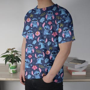 Pu&ograve; includere: T-shirt blu navy con un motivo ripetuto di un personaggio dei cartoni animati blu, fiori rosa e foglie verdi. La maglietta ha maniche corte e girocollo.