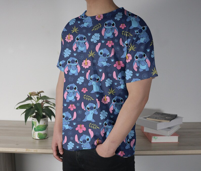 Pu&ograve; includere: T-shirt blu navy con un motivo ripetuto di un personaggio dei cartoni animati blu, fiori rosa e foglie verdi. La maglietta ha maniche corte e girocollo.