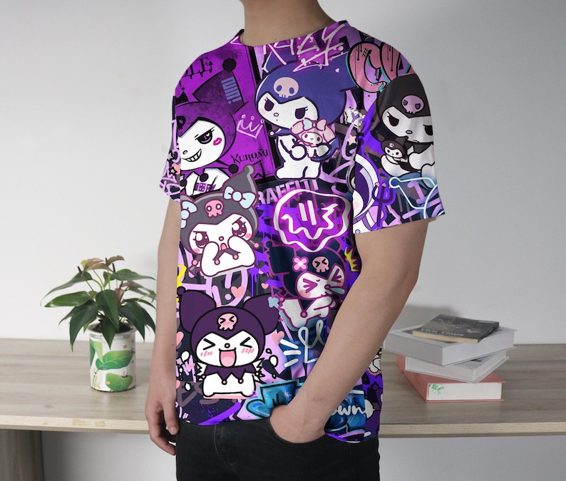May include: A purple t-shirt with a vibrant graphic design of cartoon characters and graffiti-style text. The shirt has a crew neck and short sleeves. The design features characters in purple, white, and black, creating a bold visual statement.
