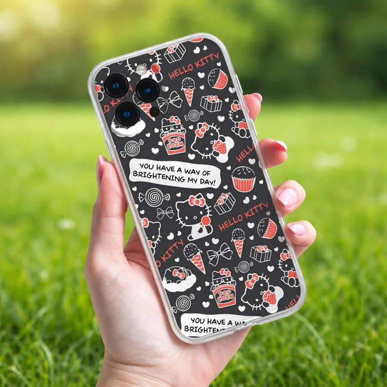 May include: A clear phone case featuring a black background with a repeating pattern of Hello Kitty characters, bows, cupcakes, ice cream cones, and popcorn. The case also includes the text "HELLO KITTY" and "YOU HAVE A WAY OF BRIGHTENING MY DAY!"