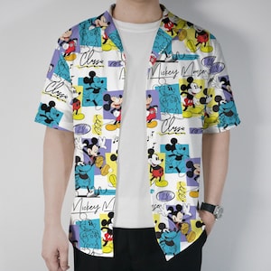 May include: White button-up shirt with a colorful Mickey Mouse pattern. The shirt features short sleeves and a classic collar. The design includes Mickey Mouse in various poses, with the words "Mickey Mouse" and "Classic" in a handwritten style.
