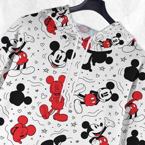 May include: White hoodie with a repeating pattern of Mickey Mouse characters in red, black, and white. The design includes hearts, stars, and other shapes. The hoodie is suspended on a black hanger.