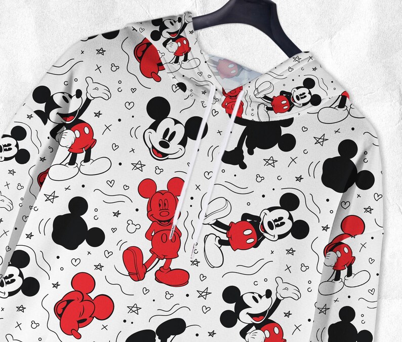 May include: White hoodie with a repeating pattern of Mickey Mouse characters in red, black, and white. The design includes hearts, stars, and other shapes. The hoodie is suspended on a black hanger.