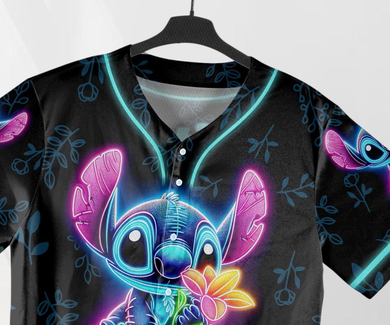 Puede incluir: Una camiseta de b&eacute;isbol negra con un personaje Stitch de color azul ne&oacute;n y rosa sosteniendo una flor. El fondo es negro con un patr&oacute;n floral.