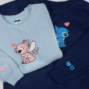 May include: Two blue and light blue sweatshirts with embroidered Stitch and Angel characters. The blue sweatshirt has a pink heart and the light blue sweatshirt has a pink heart and the letter "C".