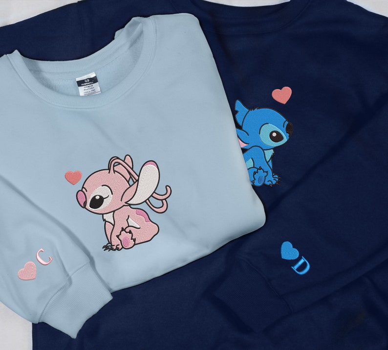 May include: Two blue and light blue sweatshirts with embroidered Stitch and Angel characters. The blue sweatshirt has a pink heart and the light blue sweatshirt has a pink heart and the letter "C".