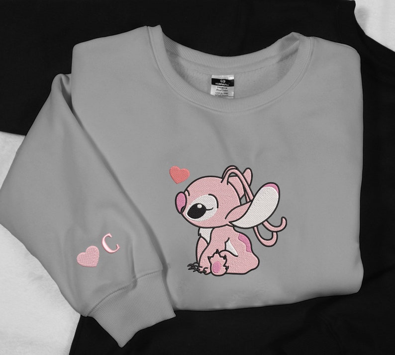 May include: Gray sweatshirt with a pink Stitch character wearing a pink heart. The sweatshirt has a pink heart and the letter C embroidered on the sleeve.