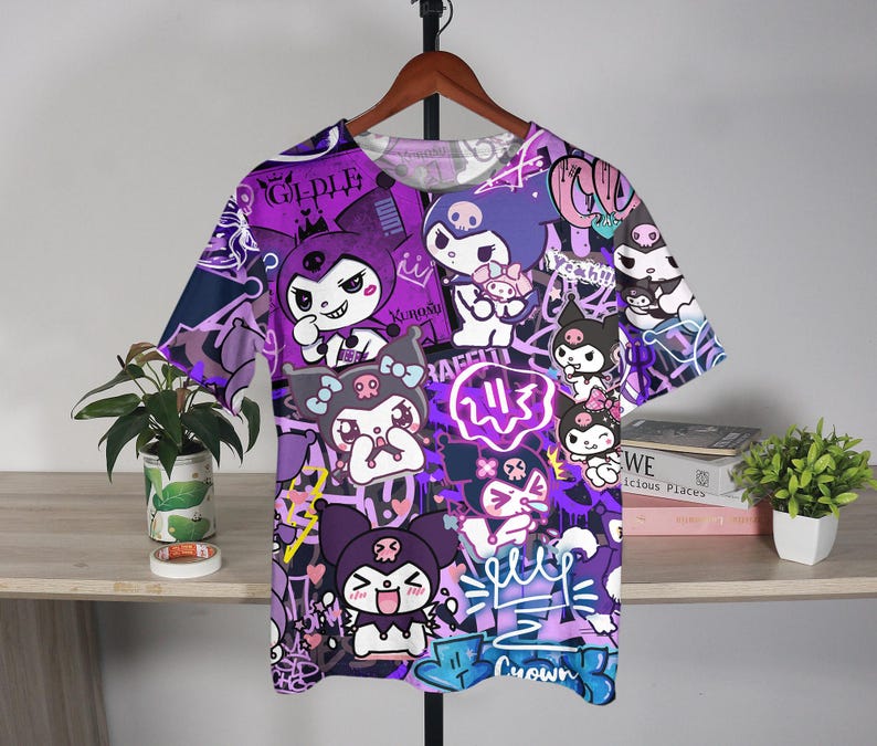 May include: A purple and white graphic t-shirt with cartoon characters and graffiti art. The t-shirt has a crew neck and short sleeves. The design includes the word "Crown" in blue and other text.
