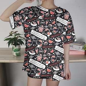 May include: Black t-shirt with a repeating pattern of Hello Kitty, cupcakes, ice cream cones, and candies. The shirt has the text "You have a way of brightening my day!" in white. The shirt is short-sleeved.