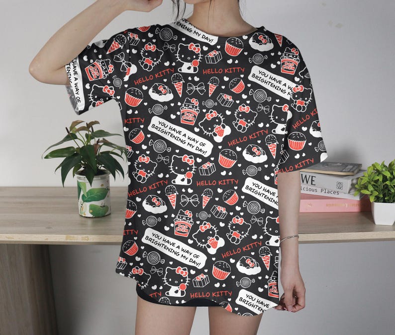 May include: Black t-shirt with a repeating pattern of Hello Kitty, cupcakes, ice cream cones, and candies. The shirt has the text "You have a way of brightening my day!" in white. The shirt is short-sleeved.