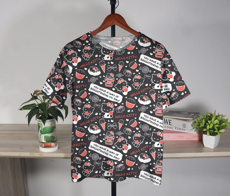 May include: Black t-shirt featuring a repeating pattern of Hello Kitty, cupcakes, ice cream cones, and candies. The shirt includes text bubbles that say "You Have a Way of Brightening My Day!" and "Hello Kitty."