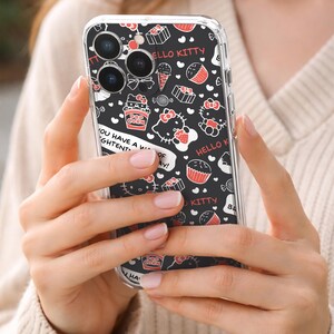 May include: Clear phone case with a black background featuring Hello Kitty illustrations, cupcakes, popcorn, and text. The case is held in a person's hands. The text on the case includes "HELLO KITTY" and "YOU HAVE A WIGHTENT OF AY!"