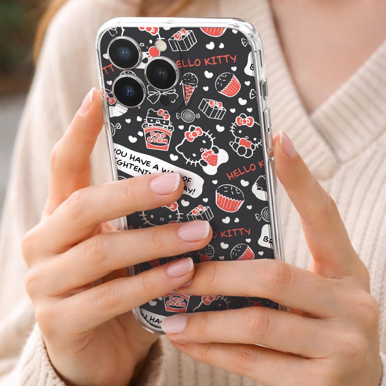 May include: Clear phone case with a black background featuring Hello Kitty illustrations, cupcakes, popcorn, and text. The case is held in a person's hands. The text on the case includes "HELLO KITTY" and "YOU HAVE A WIGHTENT OF AY!"