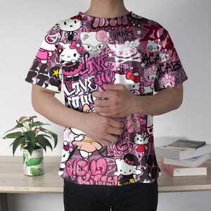 May include: A short-sleeved t-shirt with a vibrant, all-over print featuring Hello Kitty characters and graffiti-style text in shades of pink, white, and black. The design includes various poses of the character and stylized lettering.
