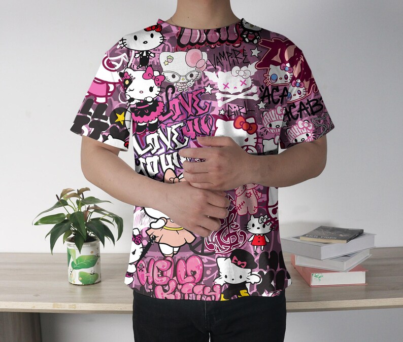 May include: A short-sleeved t-shirt with a vibrant, all-over print featuring Hello Kitty characters and graffiti-style text in shades of pink, white, and black. The design includes various poses of the character and stylized lettering.