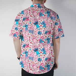 Puede incluir: Camisa de manga corta con un estampado repetido de personajes de dibujos animados azules y rosas, corazones y la palabra "LOVE" sobre un fondo blanco. La camisa est&aacute; hecha de tela ligera.