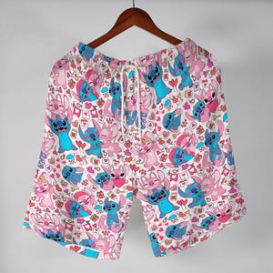 Puede incluir: Shorts blancos con un patr&oacute;n repetido de personajes de dibujos animados azules y rosas, corazones y otros gr&aacute;ficos peque&ntilde;os. Los shorts tienen cintura con cord&oacute;n y cuelgan de una percha de madera.