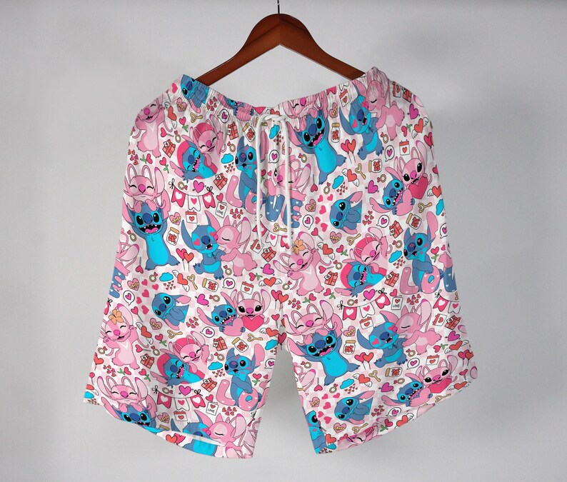 Puede incluir: Shorts blancos con un patr&oacute;n repetido de personajes de dibujos animados azules y rosas, corazones y otros gr&aacute;ficos peque&ntilde;os. Los shorts tienen cintura con cord&oacute;n y cuelgan de una percha de madera.