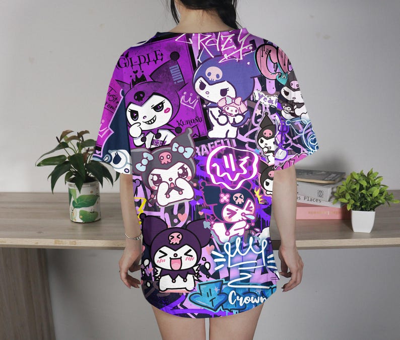 May include: A purple and black graphic t-shirt with cartoon characters and graffiti-style text. The design includes various characters, crowns, and the word "Crown". The shirt has short sleeves and a loose fit.