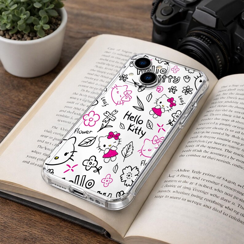 May include: Clear phone case with a Hello Kitty design. The case features a repeating pattern of Hello Kitty characters, flowers, and leaves in black and pink. The words "Hello Kitty" are also printed on the case.