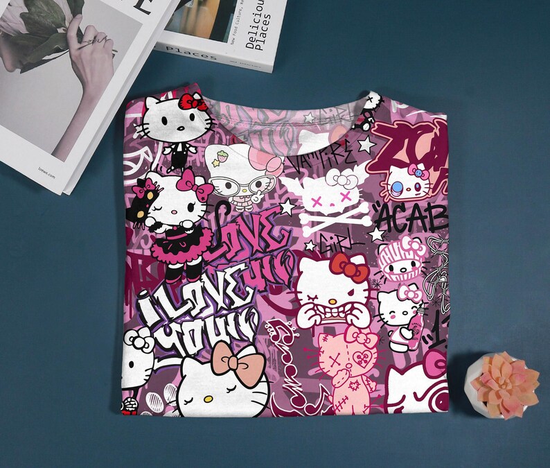 May include: A pink and purple t-shirt featuring multiple illustrations of Hello Kitty with bows and various expressions. The shirt has graffiti-style text including "I Love You" and "ACAB".