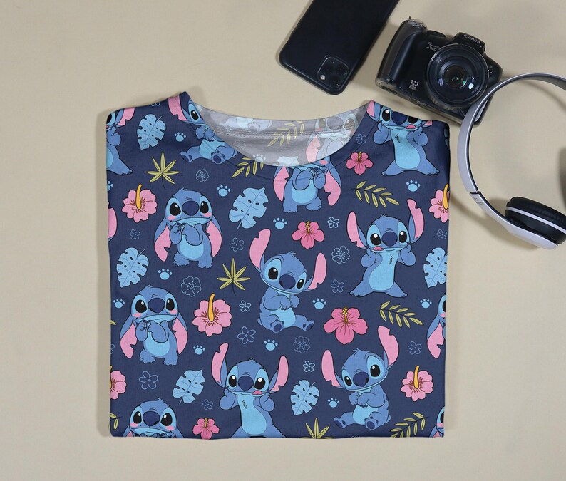 Pu&ograve; includere: Una maglietta blu navy con un motivo ripetuto del personaggio Stitch di Lilo & Stitch, fiori rosa e foglie verdi. La maglietta &egrave; a girocollo.