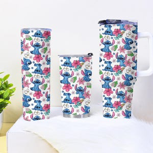 Puede incluir: Tres vasos aislados con un patr&oacute;n repetido del personaje Stitch, flores rosas y hojas verdes sobre un fondo blanco. Los vasos son de diferentes tama&ntilde;os, uno con asa.