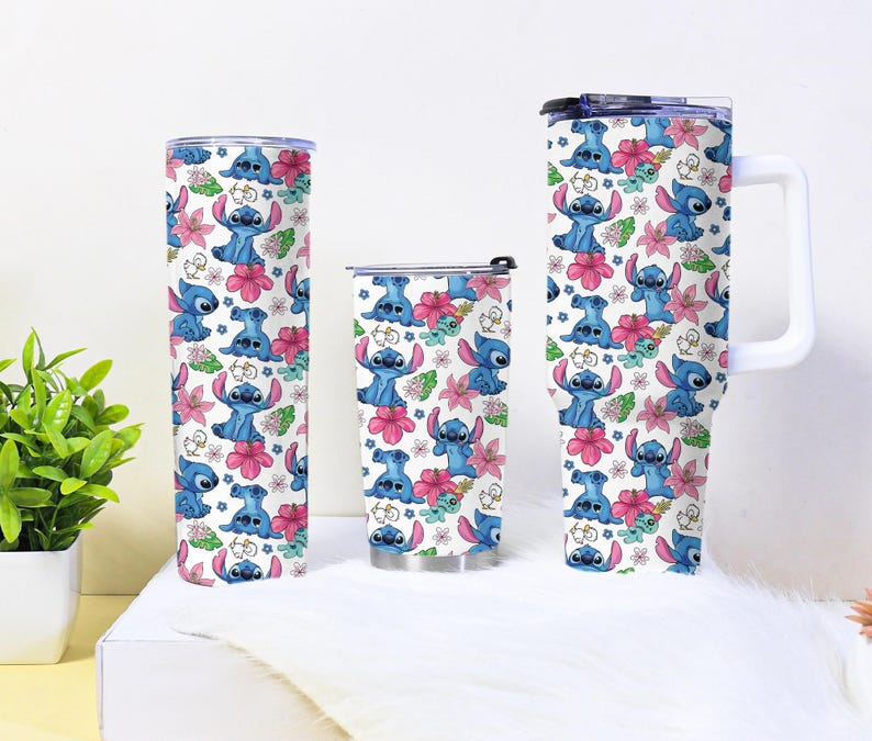 Puede incluir: Tres vasos aislados con un patr&oacute;n repetido del personaje Stitch, flores rosas y hojas verdes sobre un fondo blanco. Los vasos son de diferentes tama&ntilde;os, uno con asa.