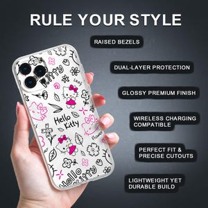 May include: Clear phone case featuring a Hello Kitty design with pink accents and black outlines. The case has a glossy finish and is decorated with flowers, bows, and the text "Hello Kitty". The case is held in a hand.