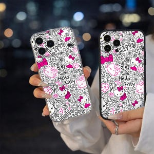 May include: Two phone cases with a white and black floral design, featuring pink Hello Kitty characters and bows. The cases have a clear and black border, with the text "Hello Kitty" throughout the design.