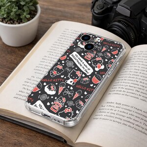 May include: A clear phone case featuring a black background with a repeating pattern of Hello Kitty characters, cupcakes, ice cream cones, and bows in red and white. The case has the text "You have a way of brightening my day!"