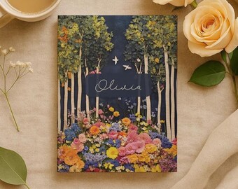 May include: A rectangular book cover featuring a forest scene with birch trees, colorful flowers, and the name "Olivia" in script. The background is a deep blue, and the flowers are in shades of pink, orange, yellow, and blue.