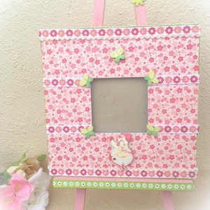 May include: Pink wooden picture frame with a floral pattern and a fairy figurine. The frame is on a small easel.